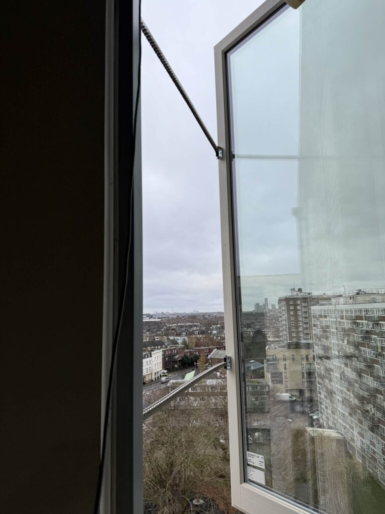 Automatic opening vent (AOV) window with the chain actuator extended, looking out over a high-rise urban landscape.