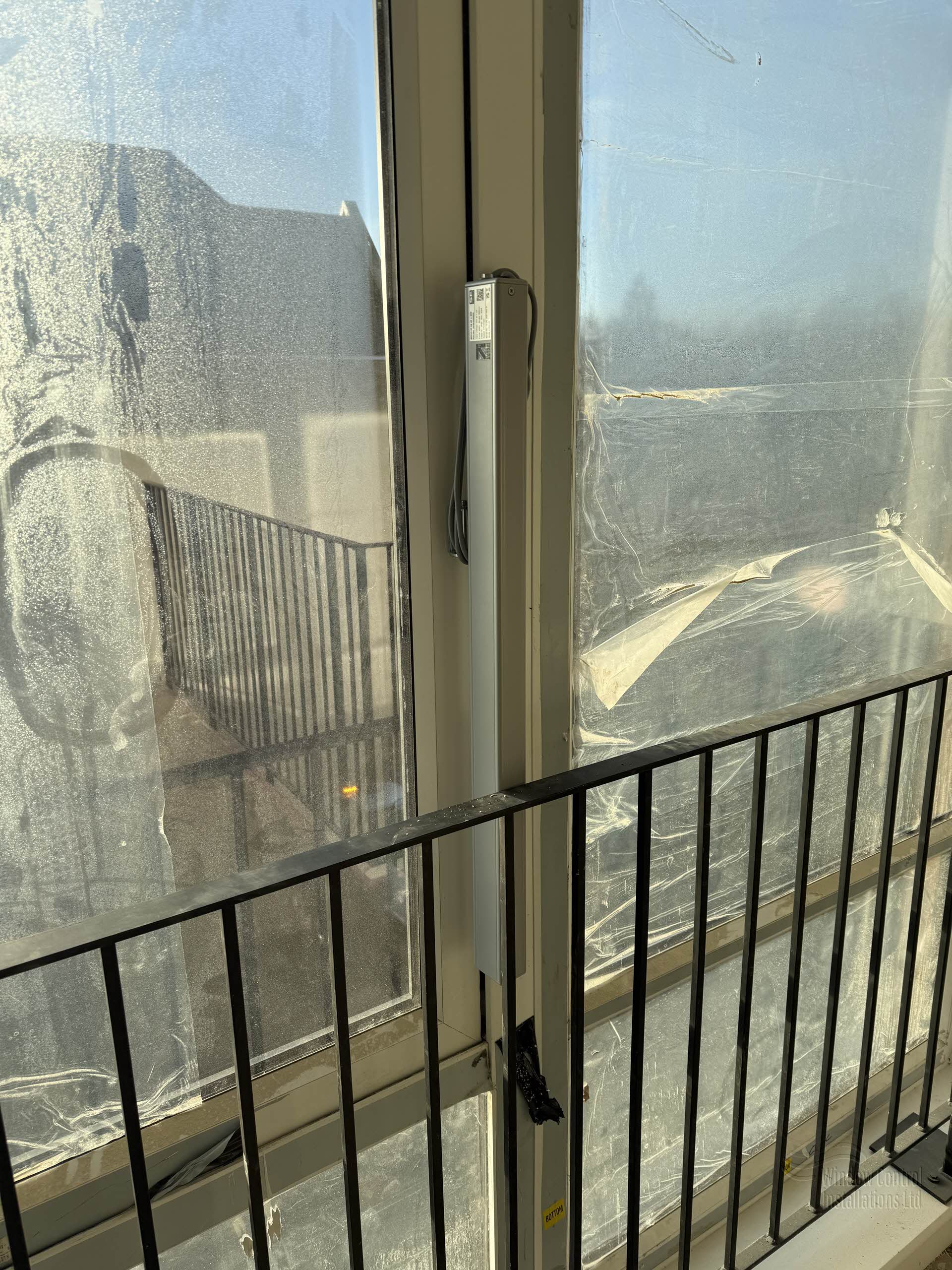 Close-up of a silver electric actuator installed on a balcony door for smoke ventilation compliance.