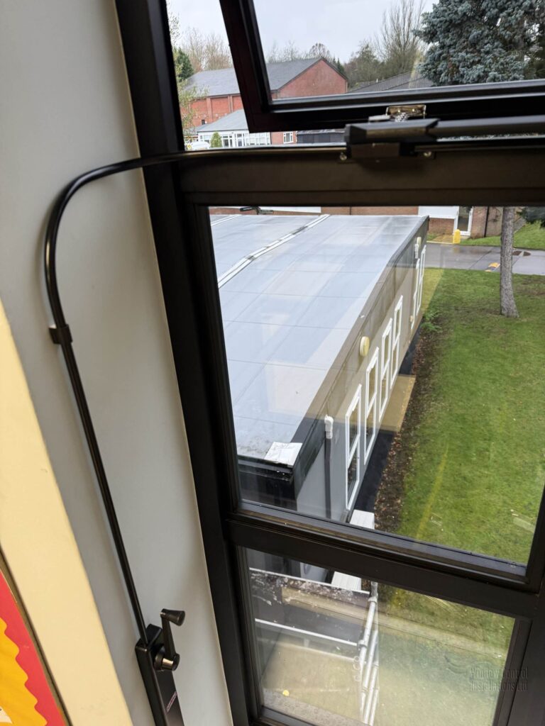 Vertical shot of a Clearline Midi operator handle and protective conduit on a window frame.