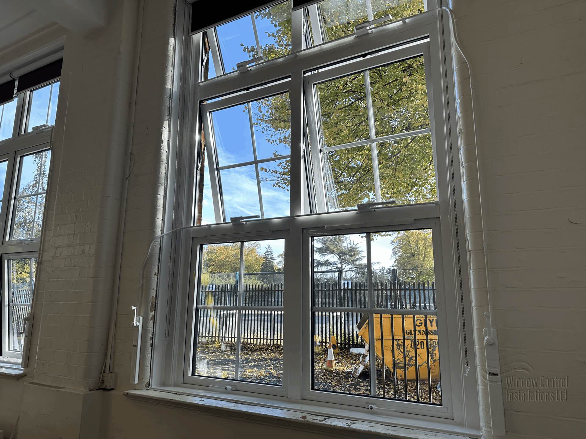 Teleflex manual window winding gear installed on a large white commercial window, showing the conduit and operator handle.