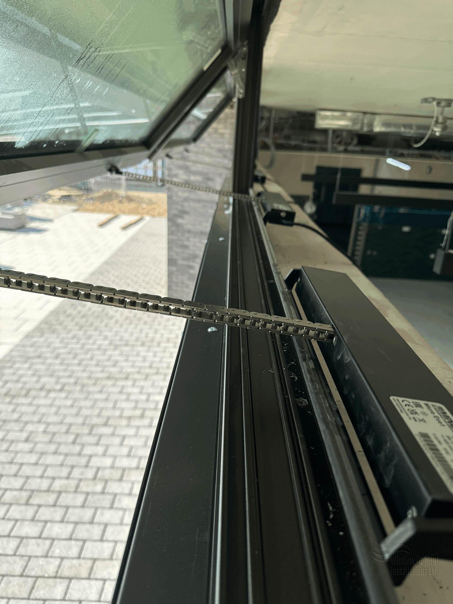 Close-up of electric chain actuator fully extended, operating a high-level commercial window for automated ventilation.
