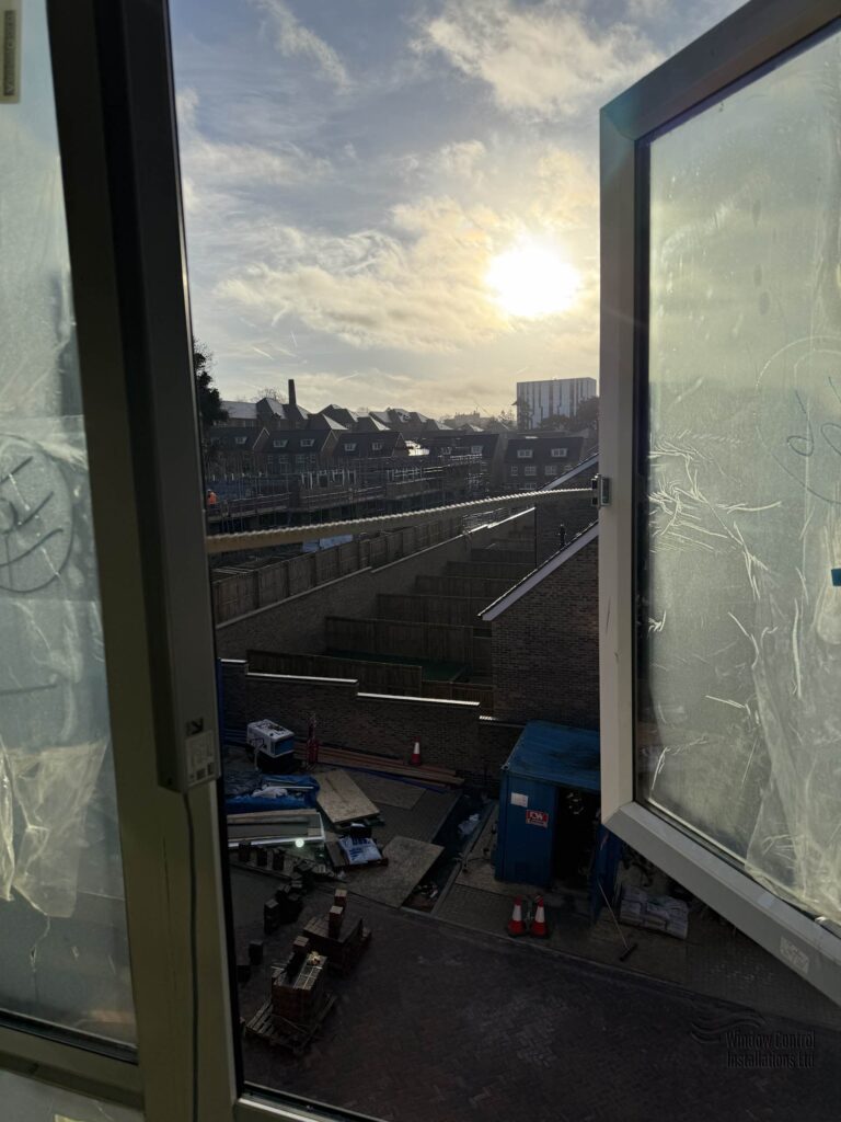 AOV smoke vent window fully opened by a chain actuator on an active residential construction site at sunset.