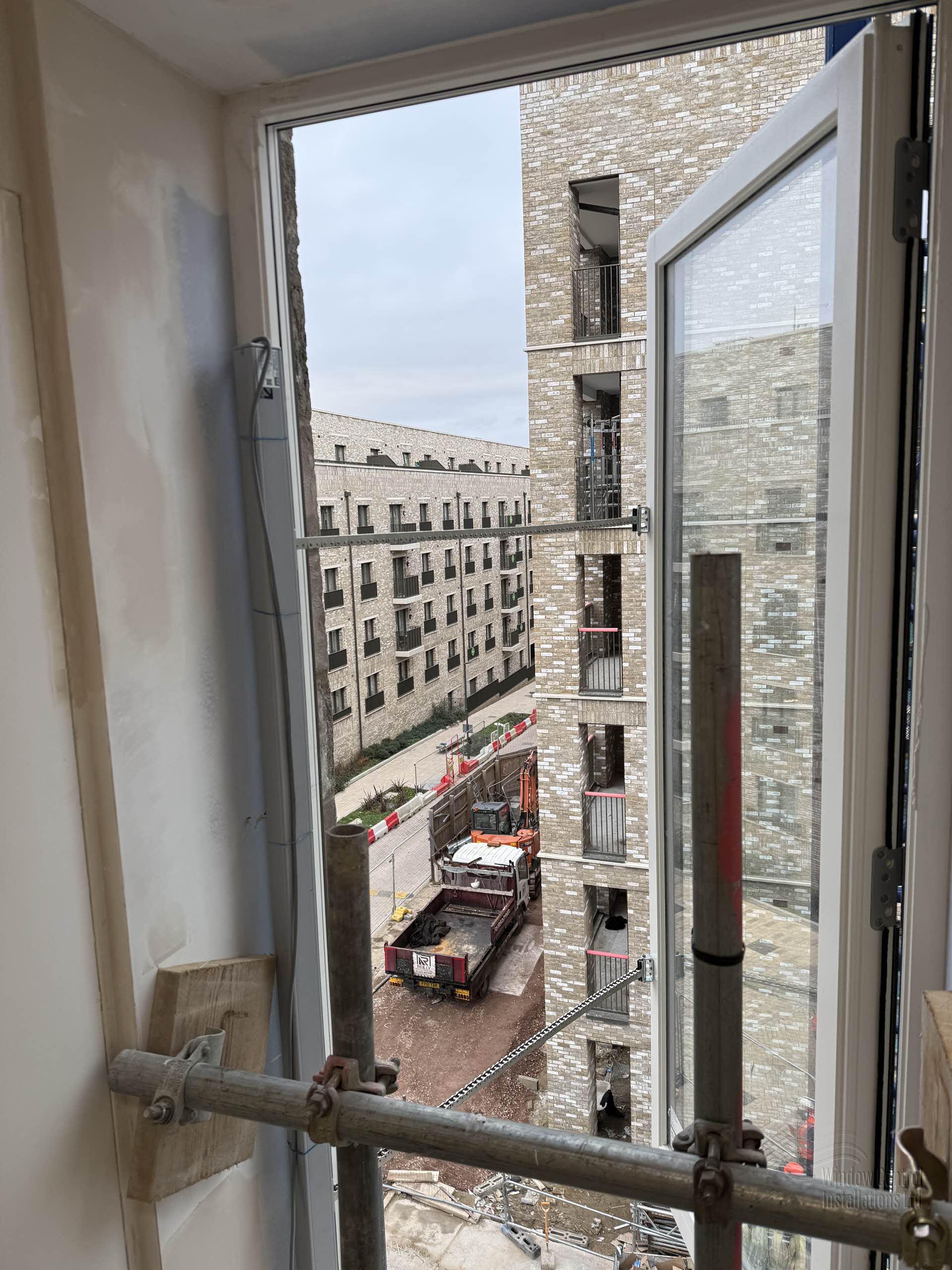 Open AOV smoke vent window overlooking a multi-story residential construction site with ongoing groundworks.