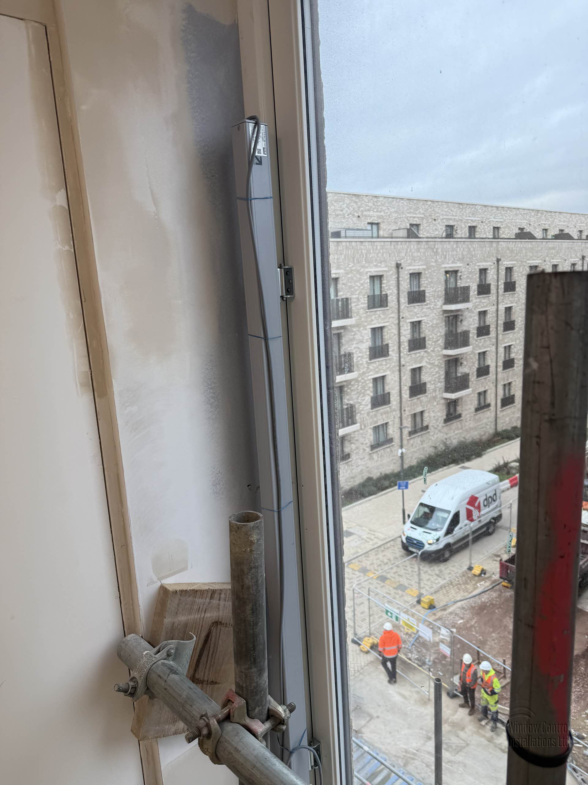 Surface-mounted silver electric chain actuator fitted to a window frame on a large housing development project.